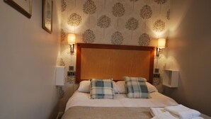 A neatly made bed with plaid pillows, a wooden headboard, and two wall-mounted lamps. - The Lion and The Lamb (Seascale)