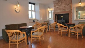 A cozy living room with a fireplace, wooden chairs, a sofa, and a round table. - The Lion and The Lamb (Seascale)