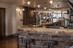 A bar area with a stone counter, multiple taps, and hanging light fixtures.