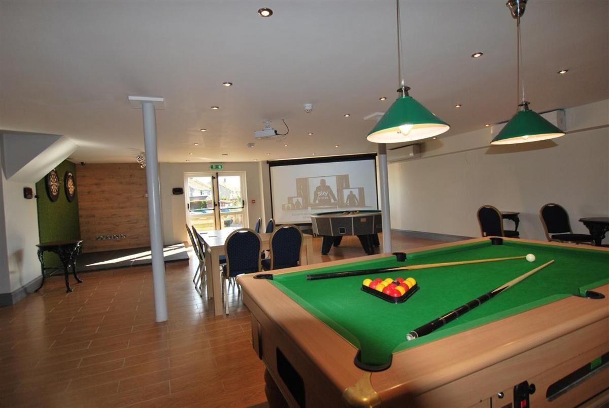 A pool table with balls, a projector screen, and a billiards table in a room with chairs and a table.