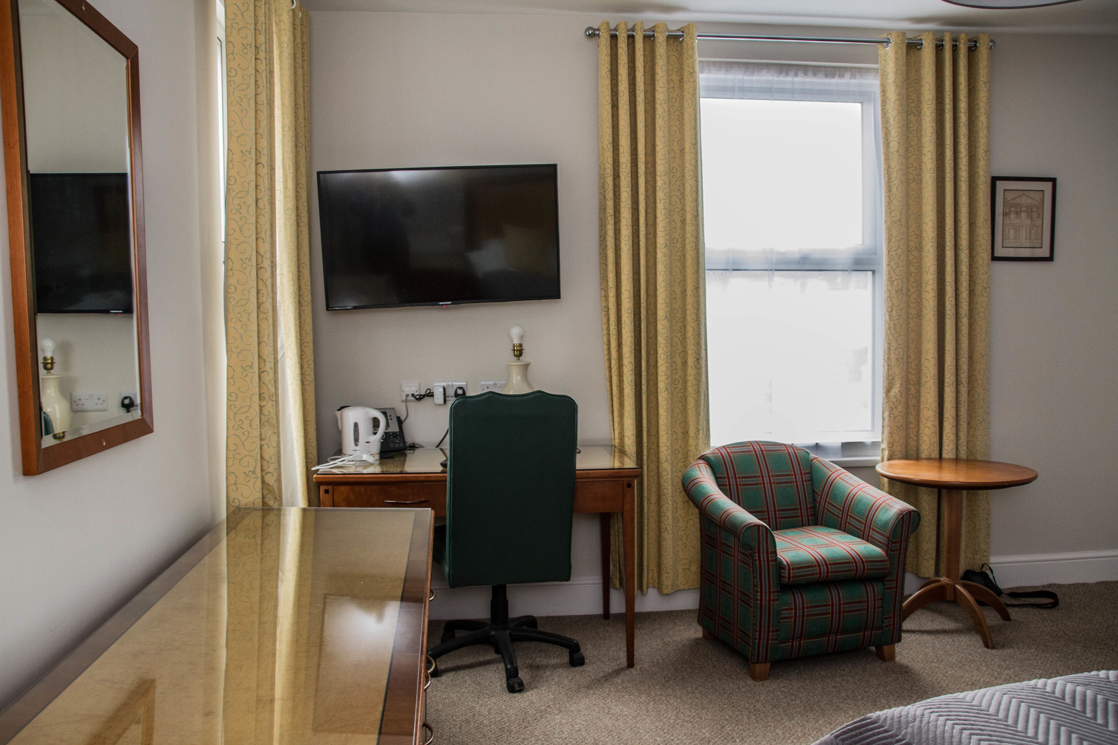 Una habitación de hotel con escritorio, silla, televisor y una pequeña mesa redonda.