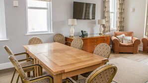 A room with a wooden dining table, wicker chairs, a sofa, a TV, and a window with curtains. - Keld Green House (Seascale)