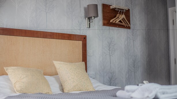A neatly made bed with a wooden headboard, two patterned pillows, and a grey blanket. - Keld Green House (Seascale)
