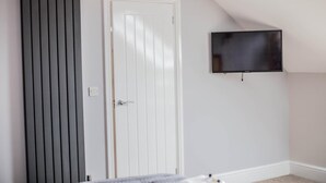 A room with a white door, a black radiator, and a mounted TV on the wall. - Keld Green House (Seascale)