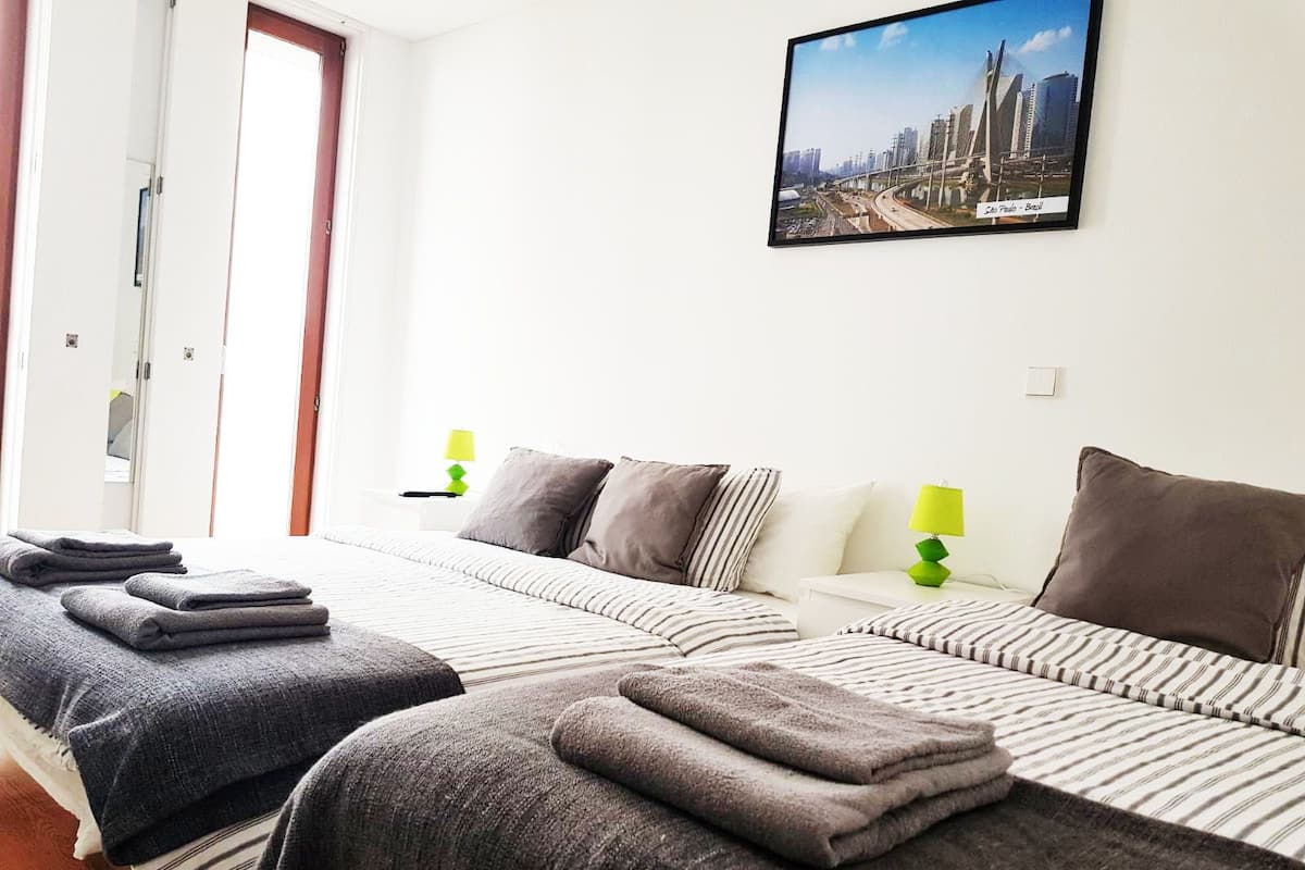 Habitación de hotel con dos camas, ropa de cama a rayas y una fotografía de un paisaje urbano en la pared.