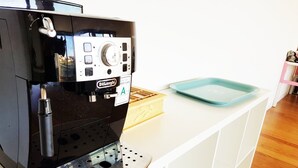 Una máquina de espresso De'Longhi con un panel de control, una bandeja azul y una caja de madera sobre una encimera blanca.