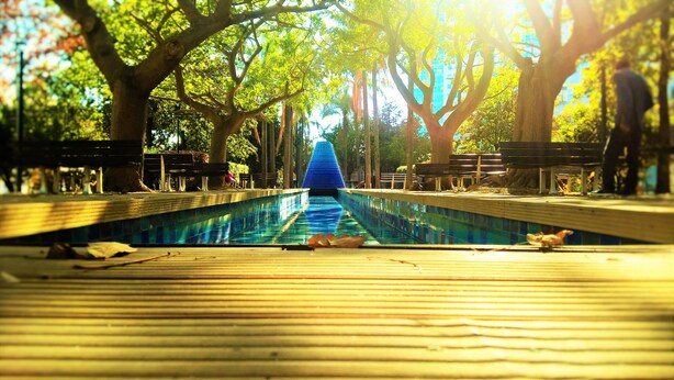 Una piscina con fuente de agua azul, rodeada de árboles y bancos.