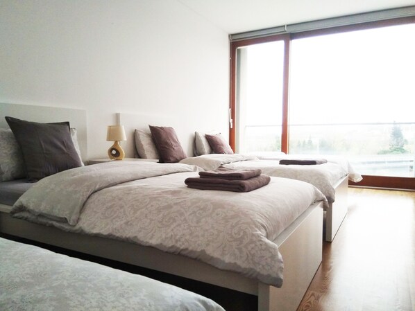 A modern bedroom with two beds, a large window, and a bedside table with a lamp. - Pantanal Hostels (Lisbon)