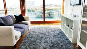 Una sala de estar con un sofá, una alfombra gris y vistas a un puente y edificios.