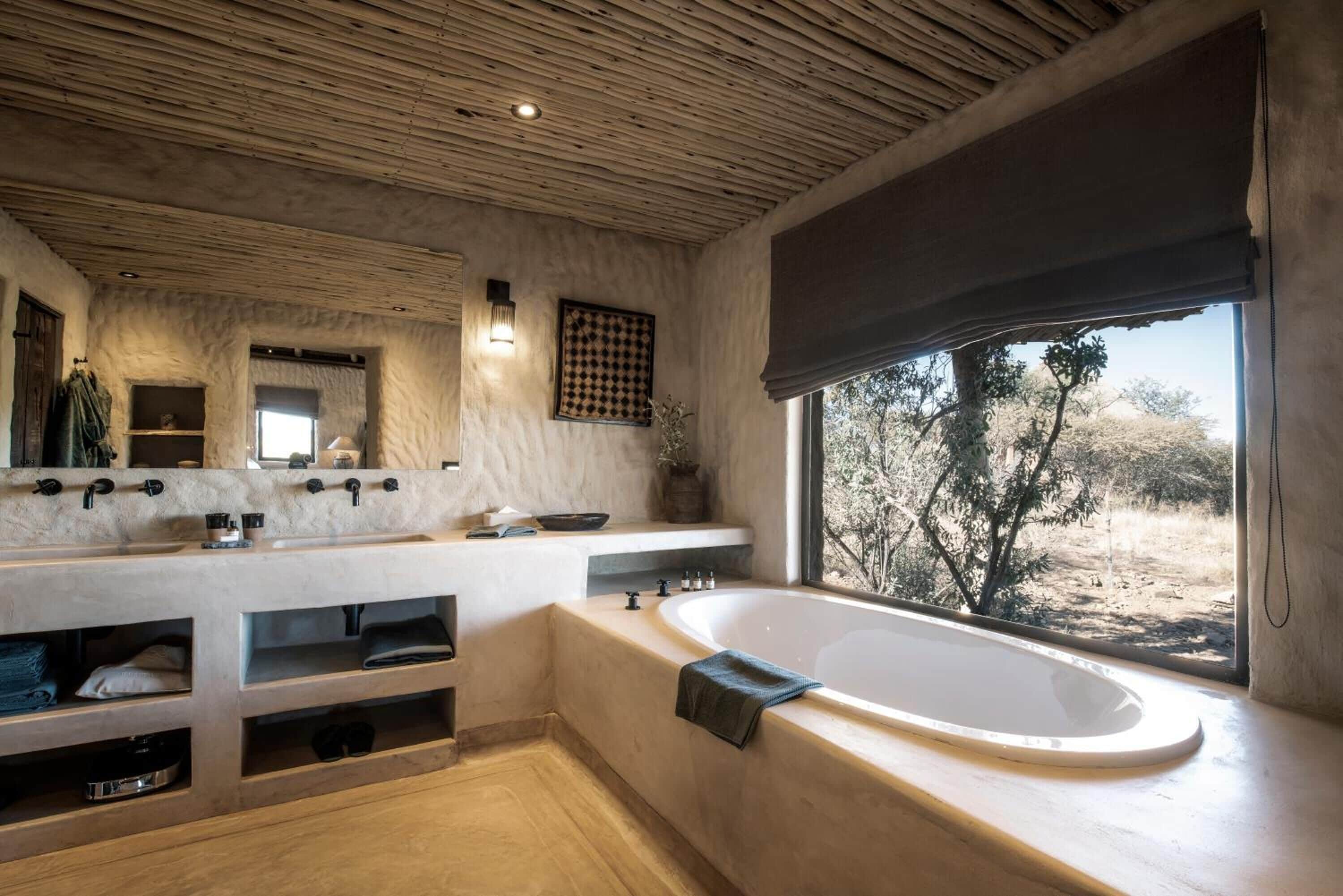 A modern bathroom with a large bathtub, a double sink vanity, and a large window offering a view of the outdoors.