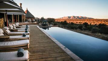 Eine Holzterrasse mit Liegestühlen und einem Pool mit Blick auf eine Wüstenlandschaft und Berge.