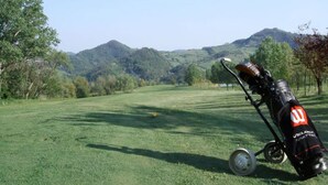 Una borsa da golf su un prato erboso, con vista su colline e alberi sullo sfondo.