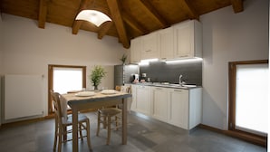 A kitchen with wooden beams, white cabinets, a dining table with chairs, and a window. - Agriturismo Mestroni (Campoformido)