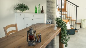 A wooden dining table with a lantern and a potted plant. A staircase with a concrete pillar and black railing is visible in the background. - Agriturismo Mestroni (Campoformido)