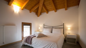 A bedroom with a wooden ceiling, a bed with white bedding, two bedside tables with lamps, and a door to the left. - Agriturismo Mestroni (Campoformido)