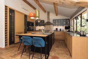 A modern kitchen with a central island, bar stools, and pendant lighting. - Domaine Les Mésanges (Gassin)