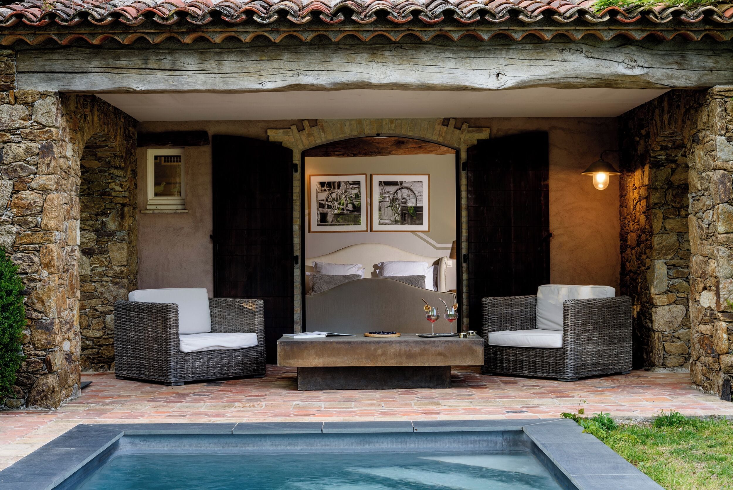 Une chambre aux murs de pierre, avec un lit, deux canapés en osier, une petite table et une piscine.