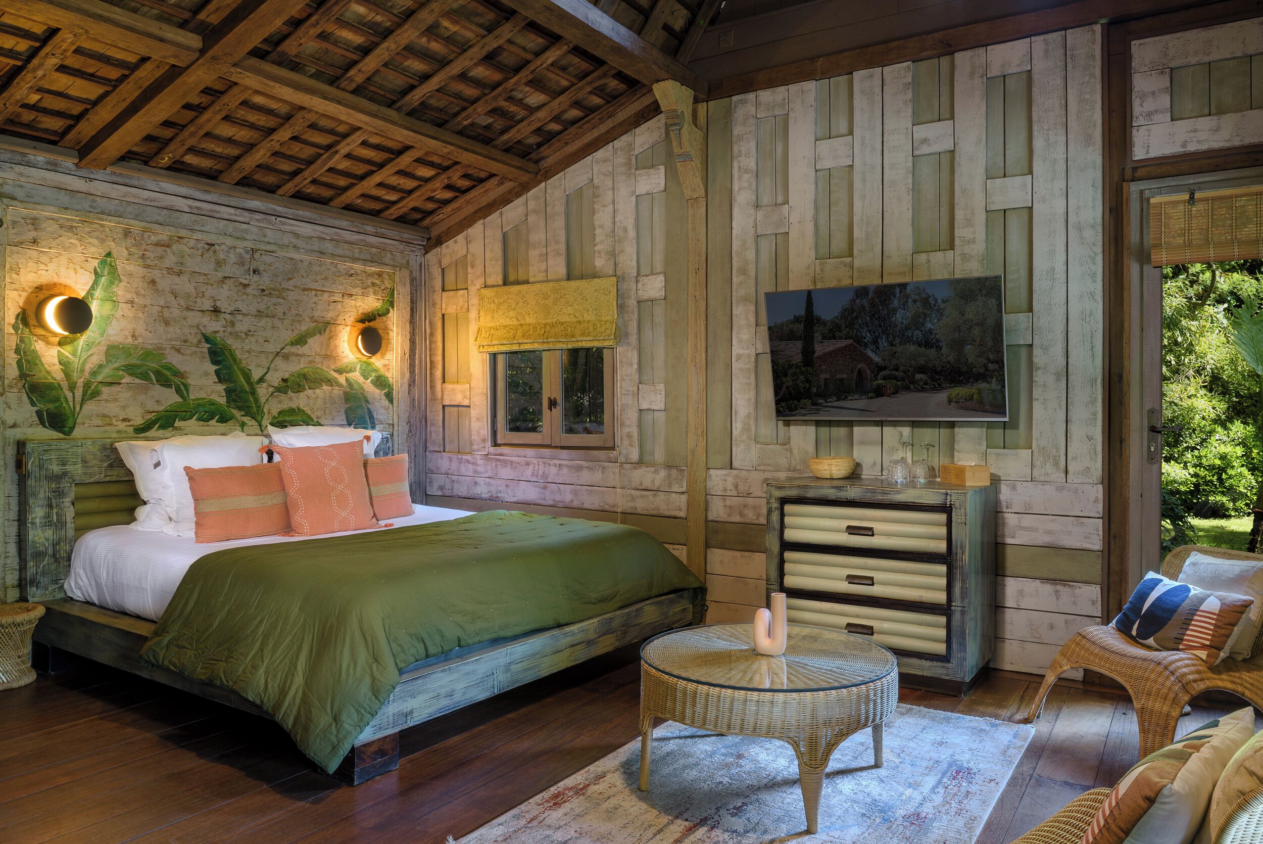 Een slaapkamer met een bed, een dressoir, een rond tafeltje en een groot raam.