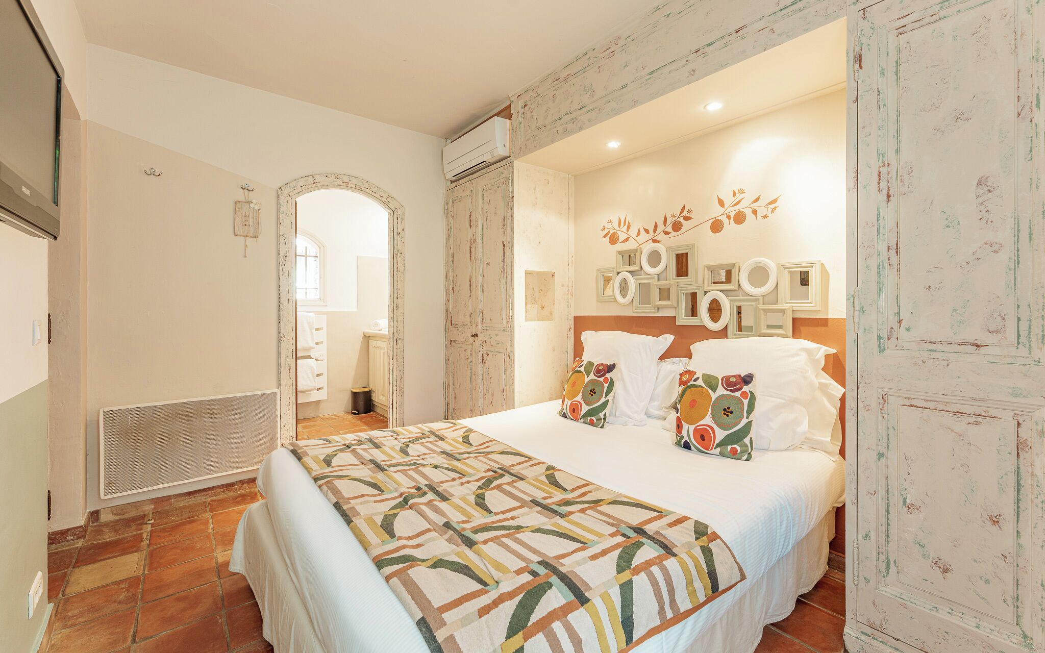 A bedroom with a bed, a headboard with wall-mounted mirrors, and a door leading to a bathroom.