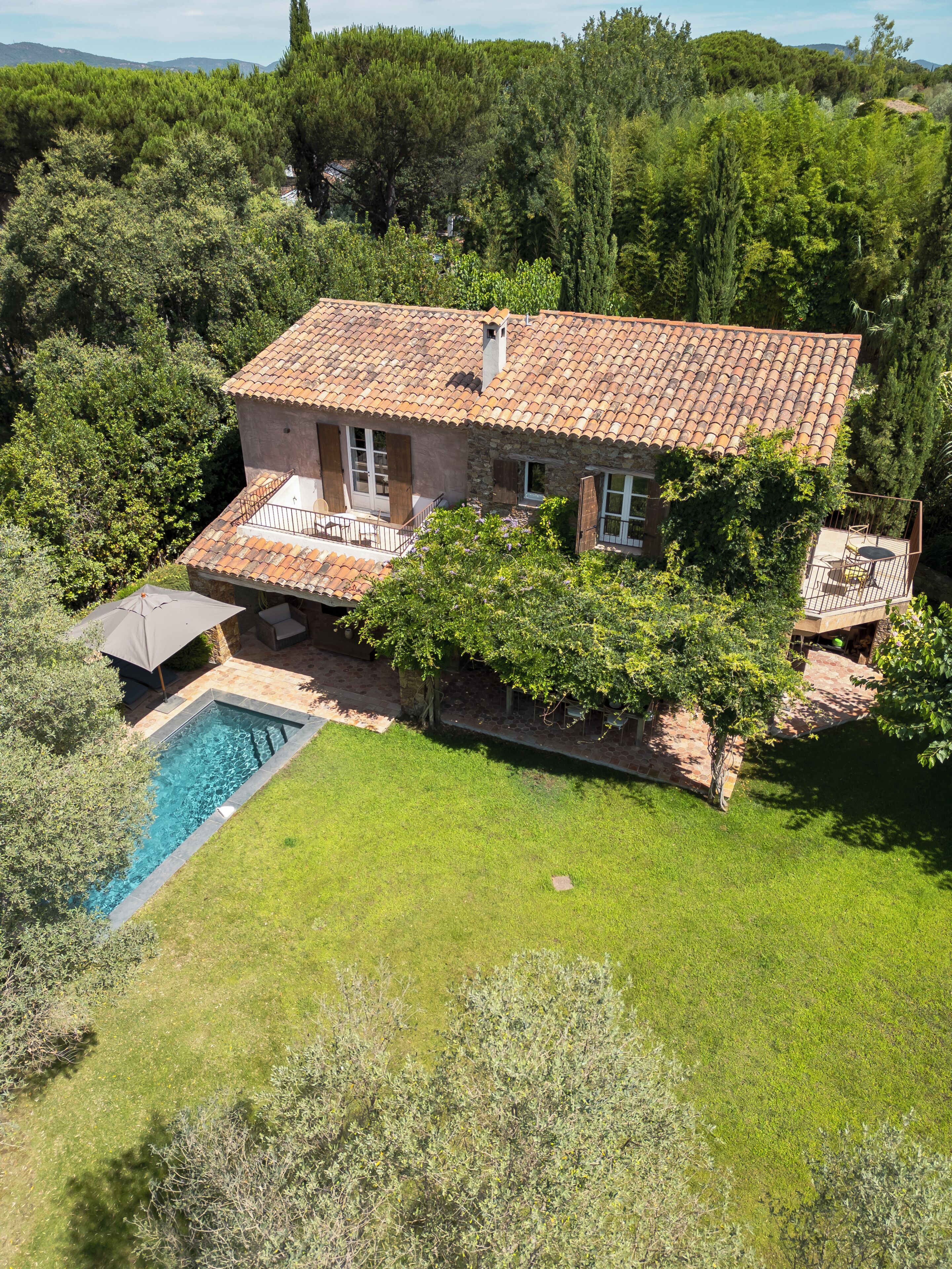 Une maison en pierre à deux étages, avec un toit en tuiles, une piscine et une pelouse bien entretenue.