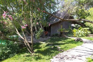 A wooden cabin with a porch, surrounded by lush greenery and flowering trees. - Domaine Les Mésanges (Gassin)