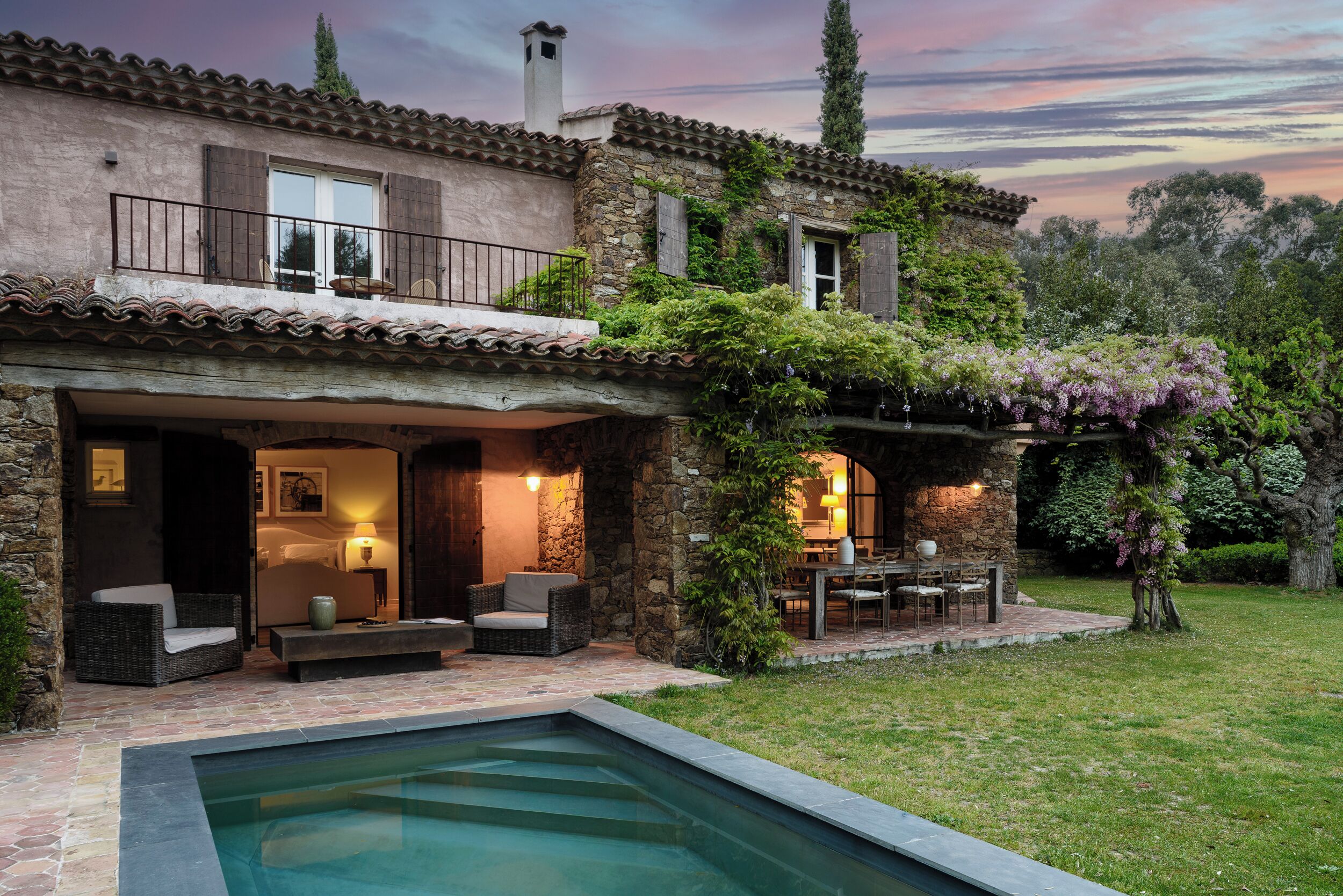 Una casa de dos pisos con fachada de piedra, piscina y mobiliario de exterior.