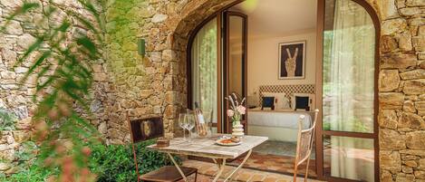Une pièce aux murs de pierre, avec un lit, une table et des chaises, et une fenêtre.