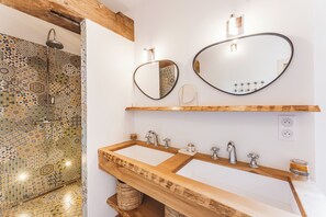 A bathroom with a wooden vanity, two sinks, and a shower with a mosaic tile wall. - Domaine Les Mésanges (Gassin)