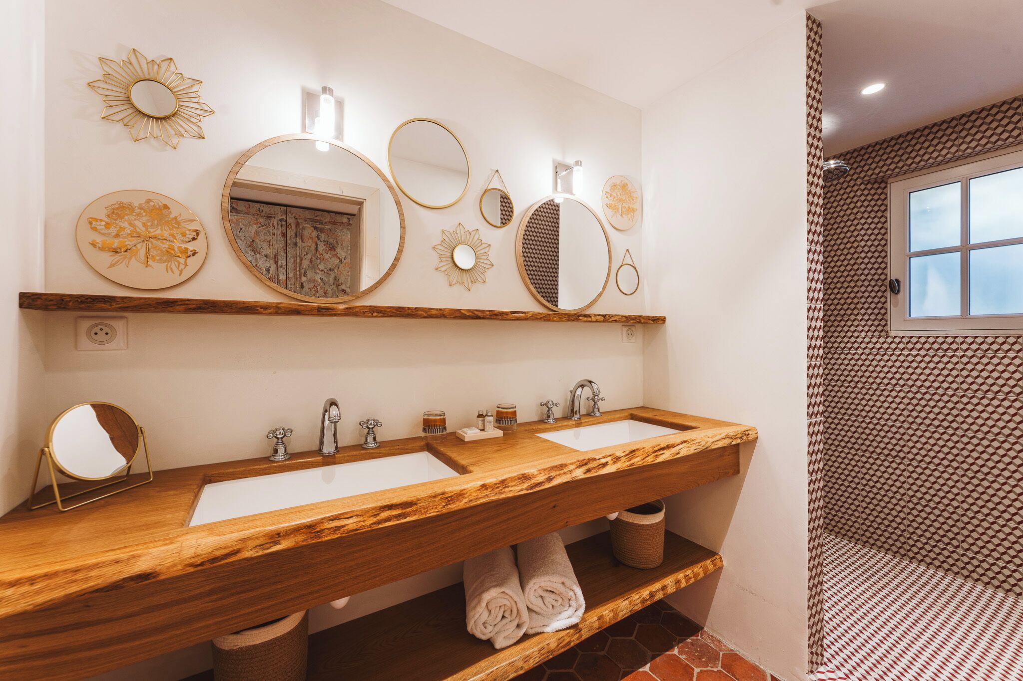 Baño con dos lavamanos, tocador de madera, espejos decorativos y pared de ducha con diseño.