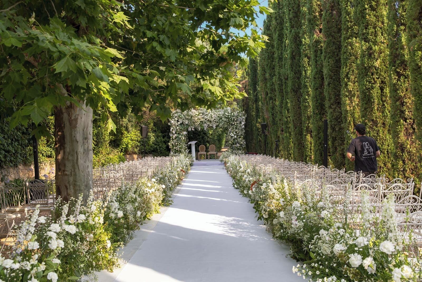 Un sentiero fiancheggiato da fiori bianchi e alberi, che conduce a una struttura ad arco.