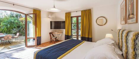A bedroom with a bed, a desk, a chair, a TV, and a view of the outdoors.