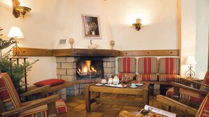 A cozy lounge area with a fireplace, striped upholstered seating, and a table set for a meal. - Hôtel Restaurant SPA Les Soldanelles (Fontcouverte-la-Toussuire)