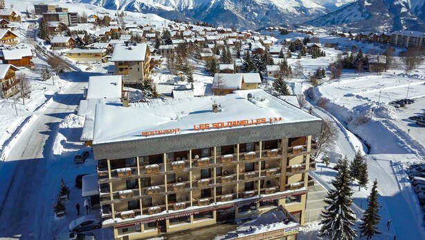 A hotel with multiple floors, outdoor seating, and a view of snow-covered mountains. - Hôtel Restaurant SPA Les Soldanelles (Fontcouverte-la-Toussuire)