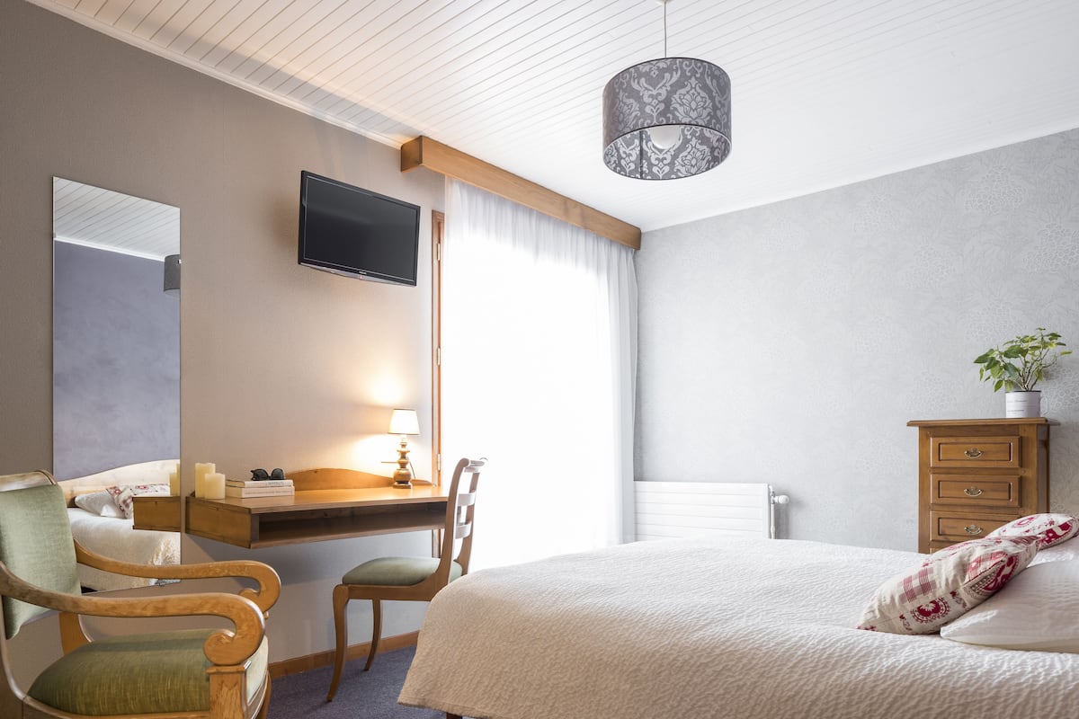Hotellihuone, jossa on sänky, työpöytä tuolilla, televisio, lipasto ja ikkuna, jossa on verhot.