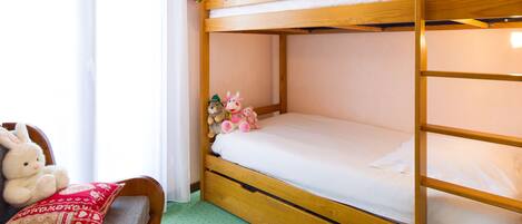 Uma cama beliche com estrutura de madeira, uma cadeira pequena com almofada e um brinquedo de pelúcia na cama.