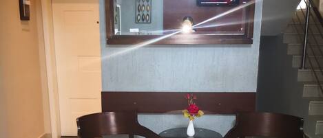 Un hall de hotel con mostrador de recepción, dos sillones tapizados, una pequeña mesa con un florero y un espejo grande que refleja la habitación.