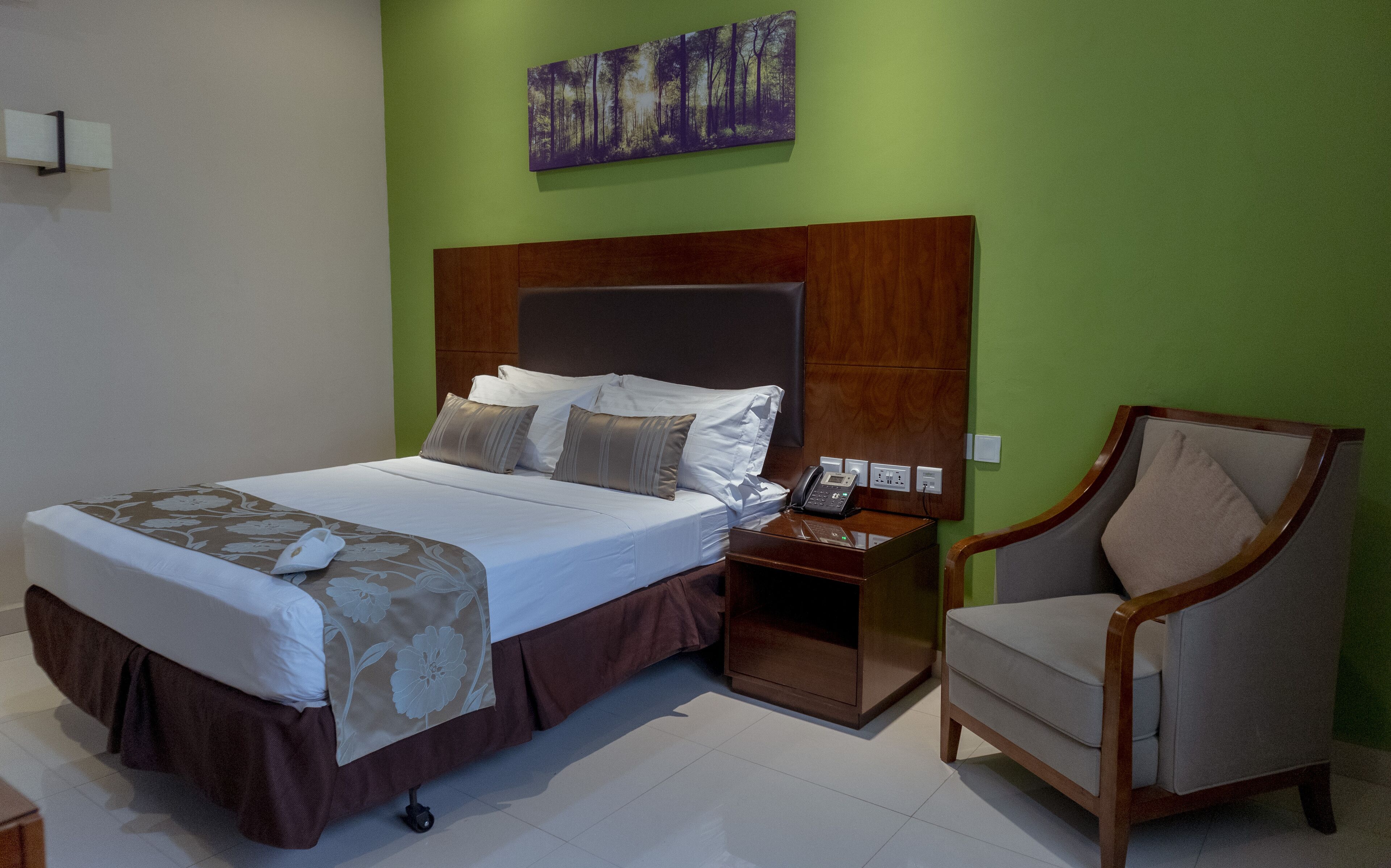 Una habitación de hotel con una cama, una silla, una mesita de noche y un cuadro en la pared.