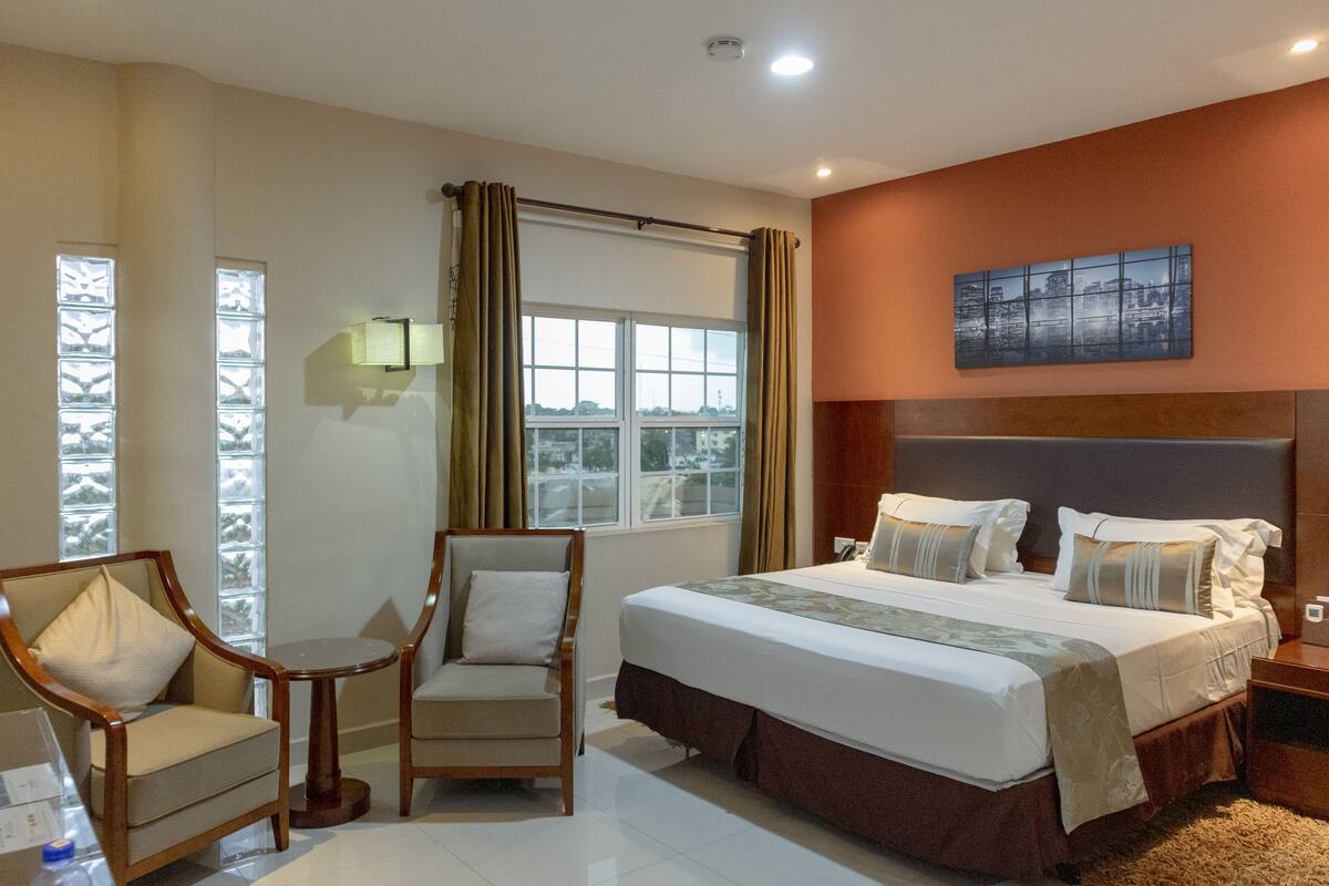 A hotel room with a large bed, two armchairs, a small table, and a window with curtains.