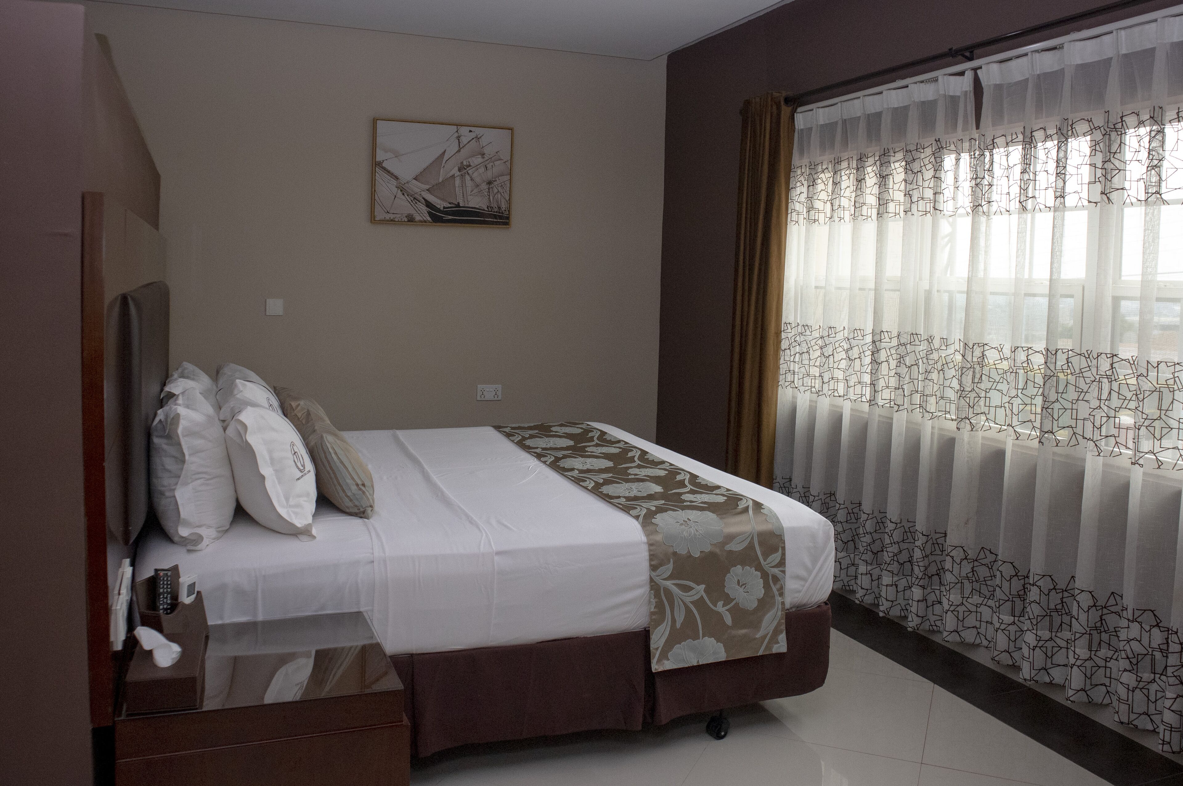 Une chambre d’hôtel avec un lit, un tableau au mur et une fenêtre avec des rideaux.