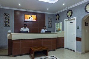 A reception desk with two staff members, a television screen, wall clocks, and a door marked "Private". - Frederick's Lodge (Kumasi)