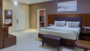 A modern hotel room with a large bed, a bedside table, a desk, and a chair. - Frederick's Lodge (Kumasi)