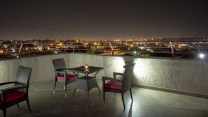 A balcony with wicker chairs and a table, overlooking a cityscape at night. - Frederick's Lodge (Kumasi)