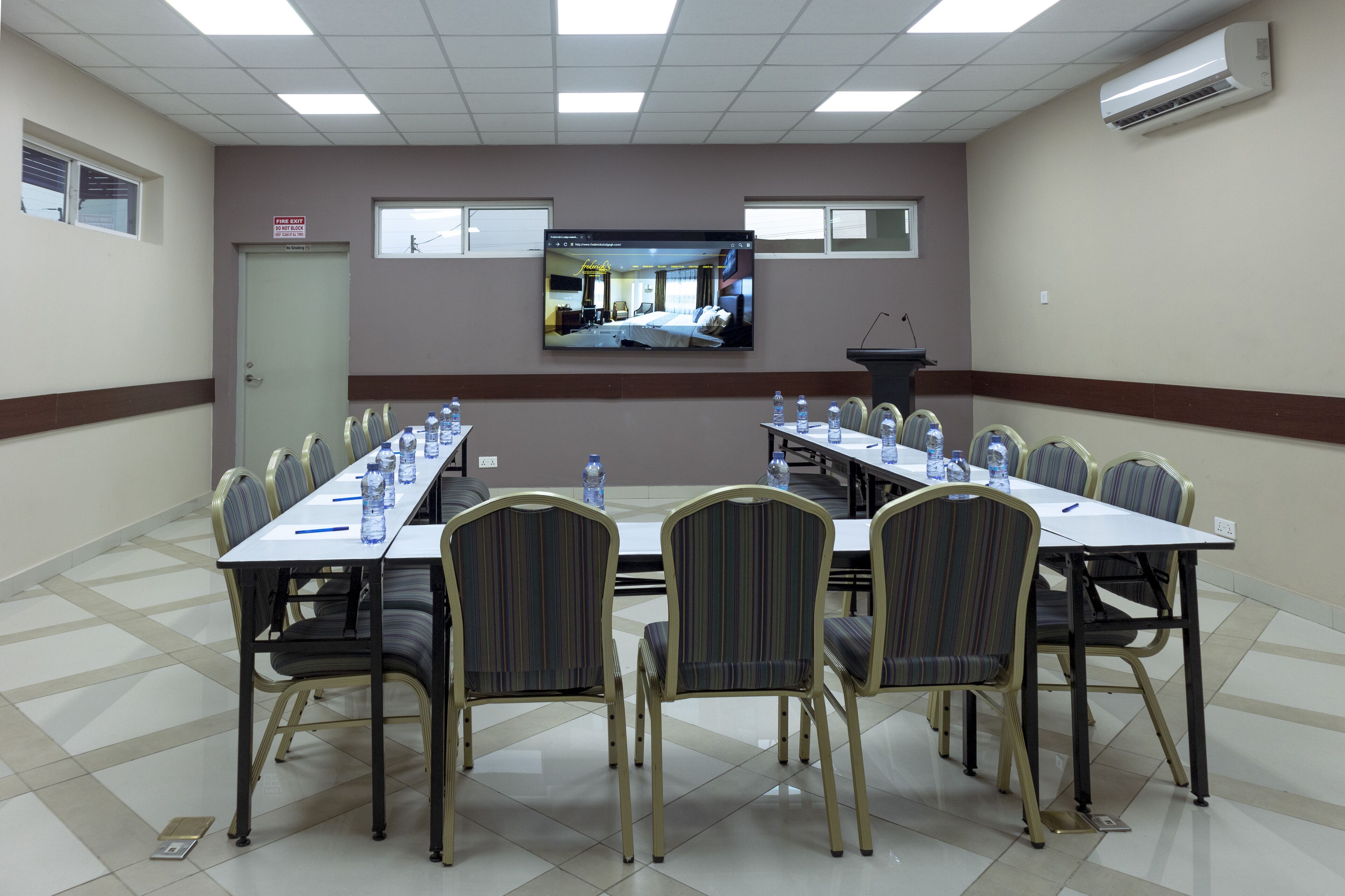 Una sala de conferencias con una larga mesa, sillas y una pantalla grande que muestra una habitación de hotel.