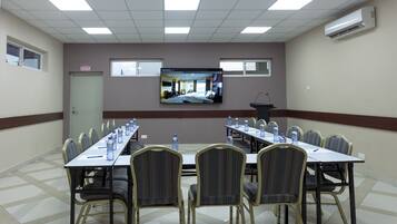 Una sala de conferencias con una larga mesa, sillas y una pantalla grande que muestra una habitación de hotel.