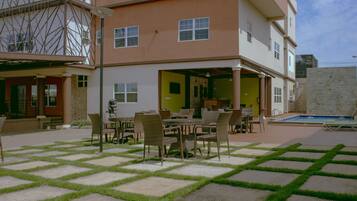 A multi-story building with a covered outdoor seating area, a pool, and a stone wall.