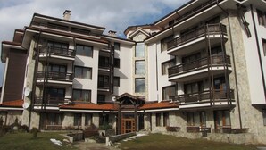 A multi-story residential building with balconies, a central entrance, and a stone facade.