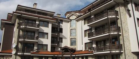 A multi-story residential building with balconies, a central entrance, and a stone facade.