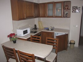 Una cocina compacta con armarios de madera, un microondas, un lavamanos y una zona de comedor con sillas.