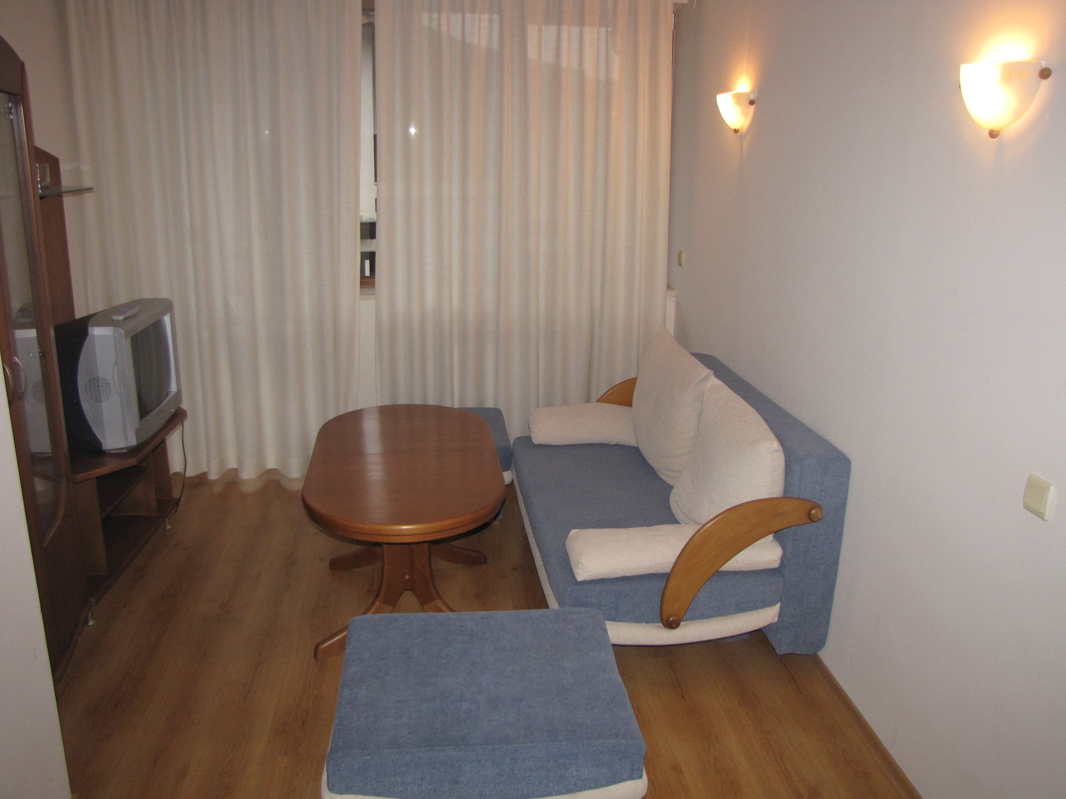A small, cozy living room with a wooden table, a blue sofa, and a television on a wooden stand.