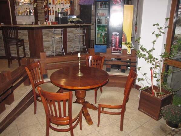 Una zona de bar con mobiliario de madera, un refrigerador lleno de bebidas y una planta en maceta.